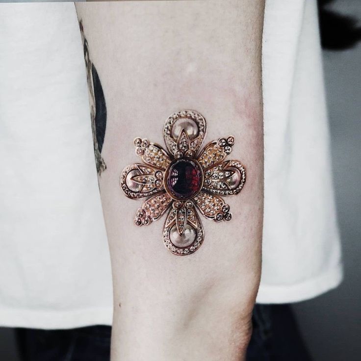 a person with a tattoo on their arm has a red stone in the center of it