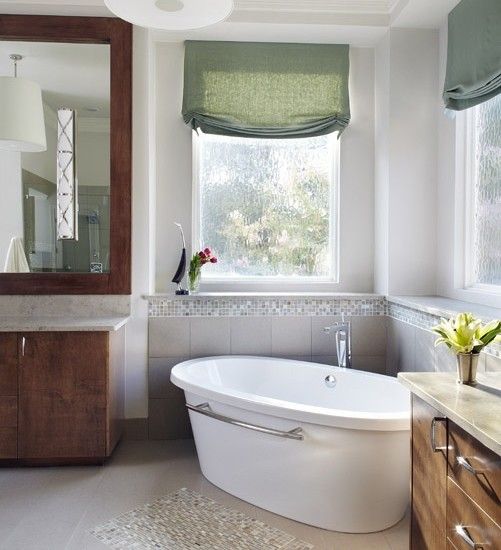 a bath tub sitting under a bathroom window next to a sink and counter with flowers on it