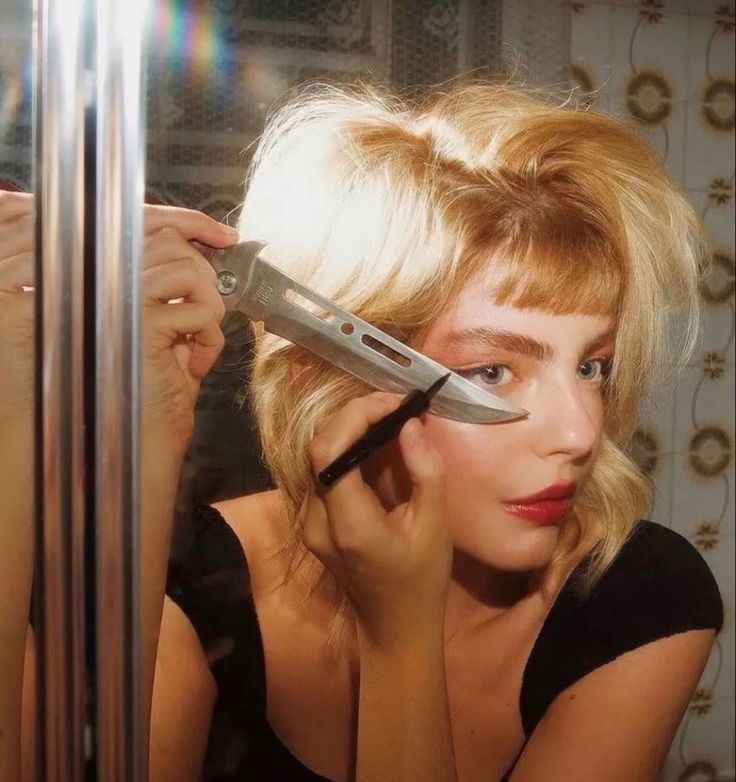 a woman holding a knife in front of her face and looking into the mirror while she is getting ready to cut her hair