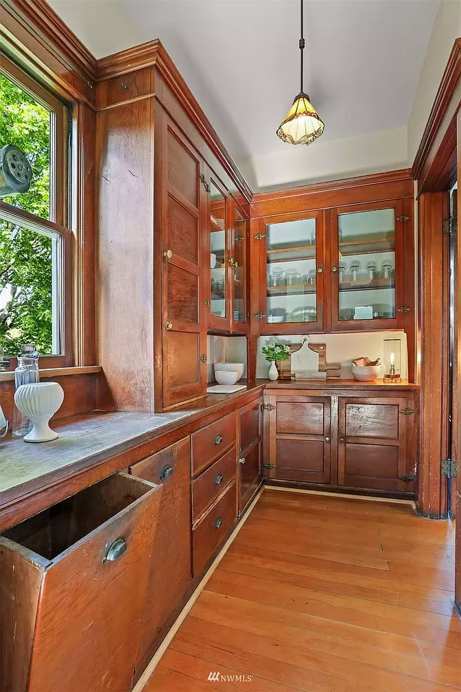 an empty kitchen with wooden cabinets and wood flooring, along with a large window