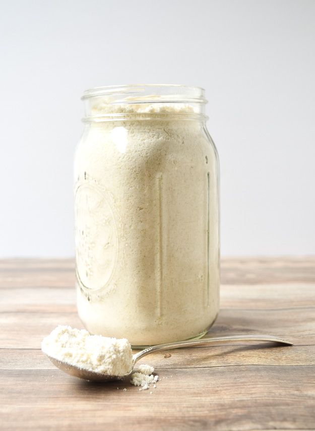 a jar filled with white powder sitting on top of a wooden table next to a spoon