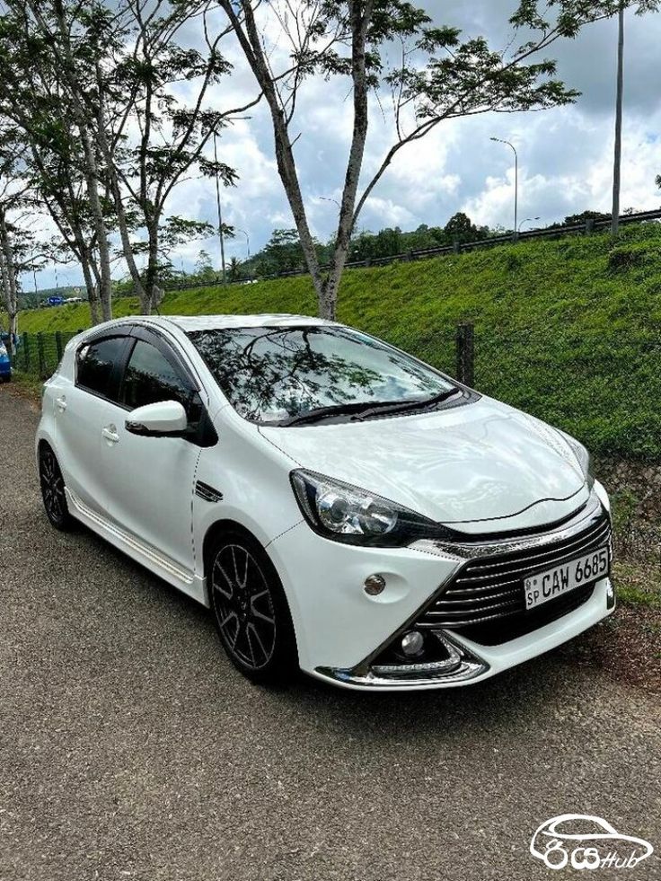 a white car parked on the side of a road next to some grass and trees