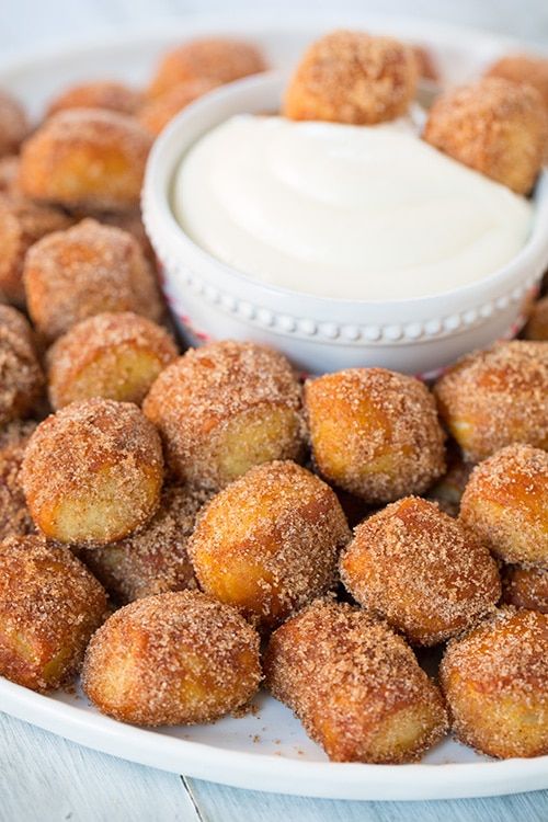 a white plate topped with sugared donuts next to a small bowl of dip