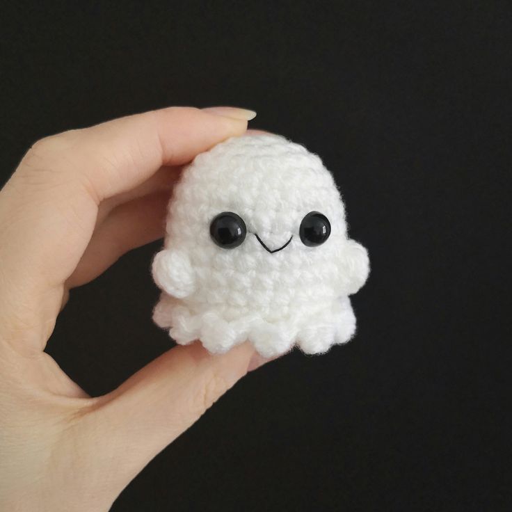 a hand holding a small white crocheted cloud with eyes on it's face