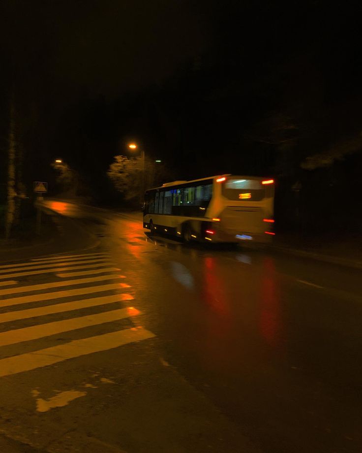 a bus is driving down the street at night with its lights on and it's raining