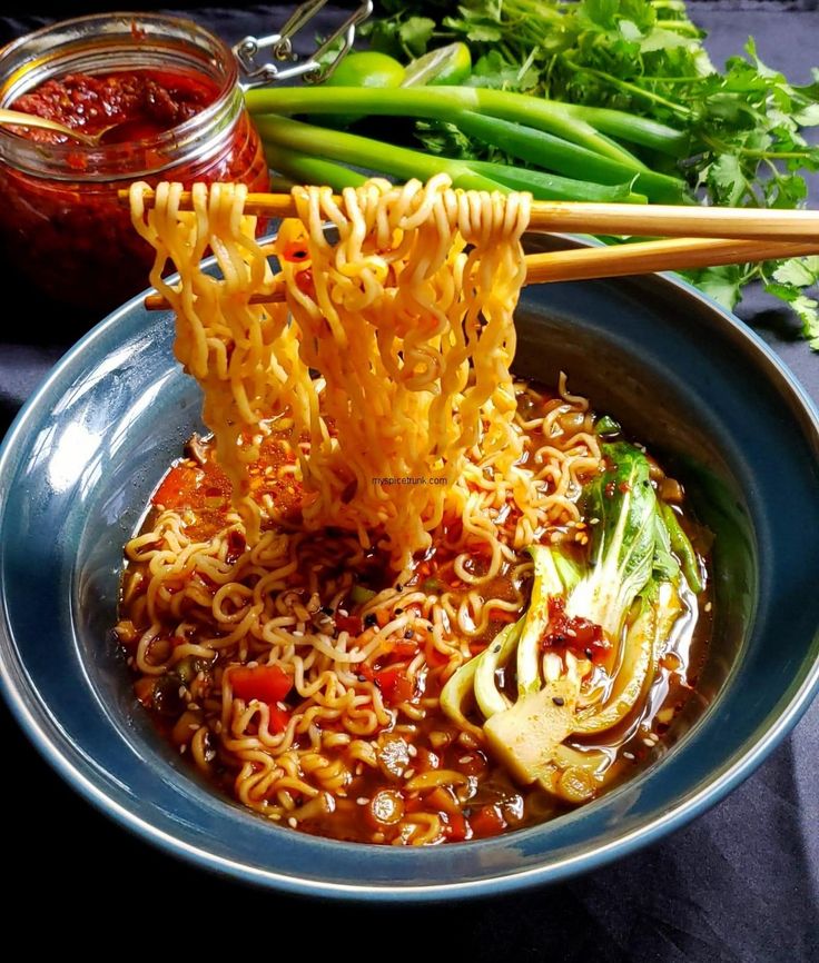 chopsticks sticking out of noodles in a bowl with vegetables and sauce on the side