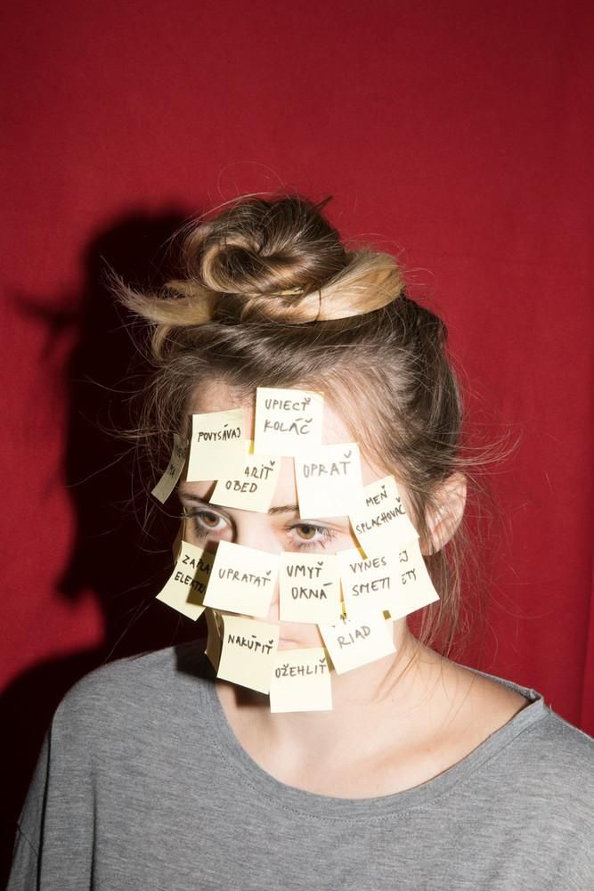 a woman with sticky notes on her face and hair pinned to her forehead, in front of a red background