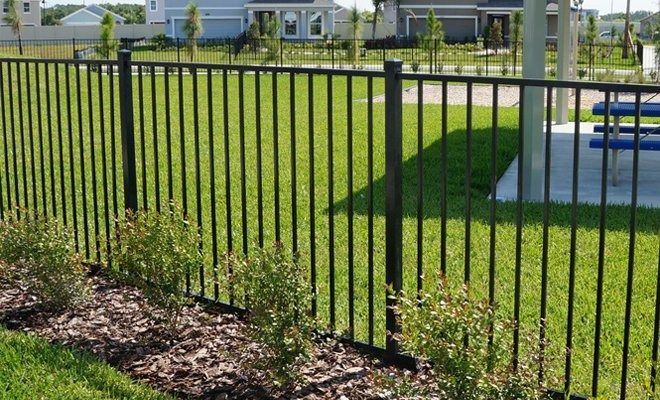 a black metal fence in the middle of a grassy area next to a swimming pool