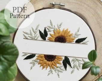 a cross stitch sunflower on a white background next to a green leafy plant