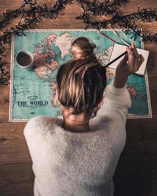 a woman writing on a world map with a cup of coffee in front of her