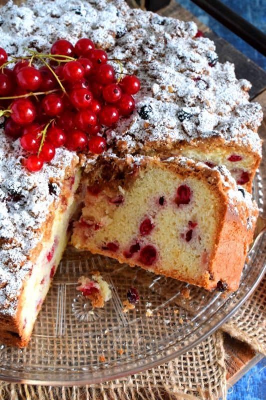 a cake on a glass plate with cherries and powdered sugar toppings is cut into slices