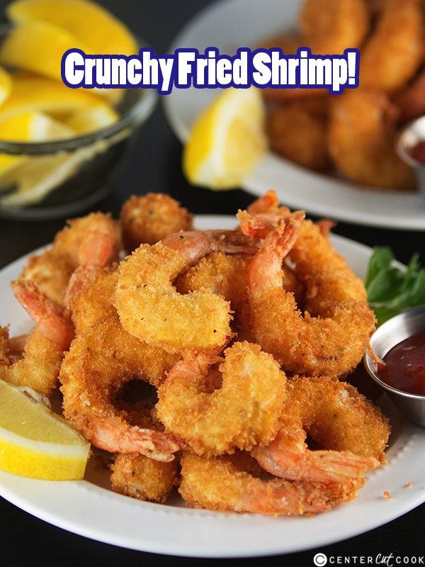 some fried shrimp on a white plate with lemon wedges and ketchup