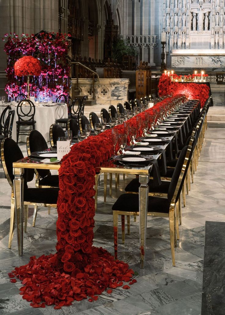 a long table is set with black chairs and red flowers on the tables in front of it