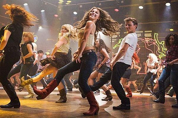 a group of people dancing on stage with lights in the background and one person wearing boots