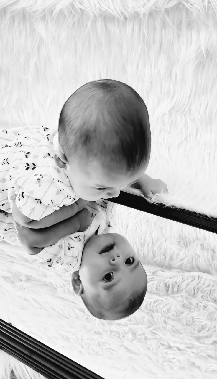 two babies are looking at each other in the mirror, and one is upside down