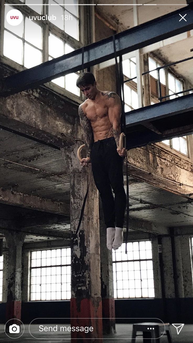 a shirtless man hanging upside down on a pole in an old building with windows