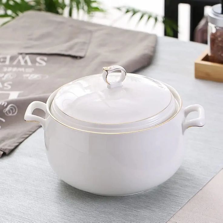 a white casserole sitting on top of a table next to a napkin and pot