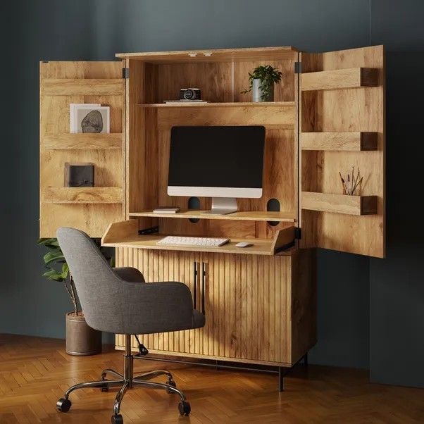 a desk with a computer on top of it in front of a bookcase and chair