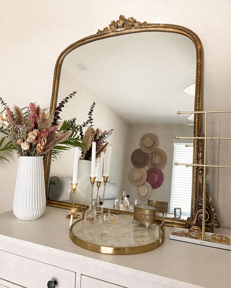 a mirror sitting on top of a white dresser next to a vase filled with flowers