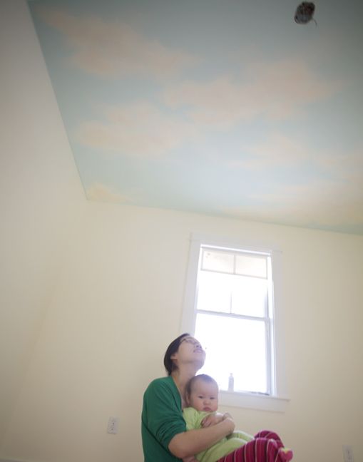 a woman holding a baby in her arms and looking up at the sky painted on the ceiling