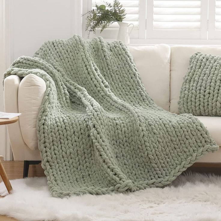 a white couch sitting next to a window covered in a green knitted throw blanket