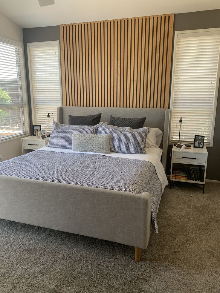 a bedroom with a bed, nightstands and two windows covered in shades of gray