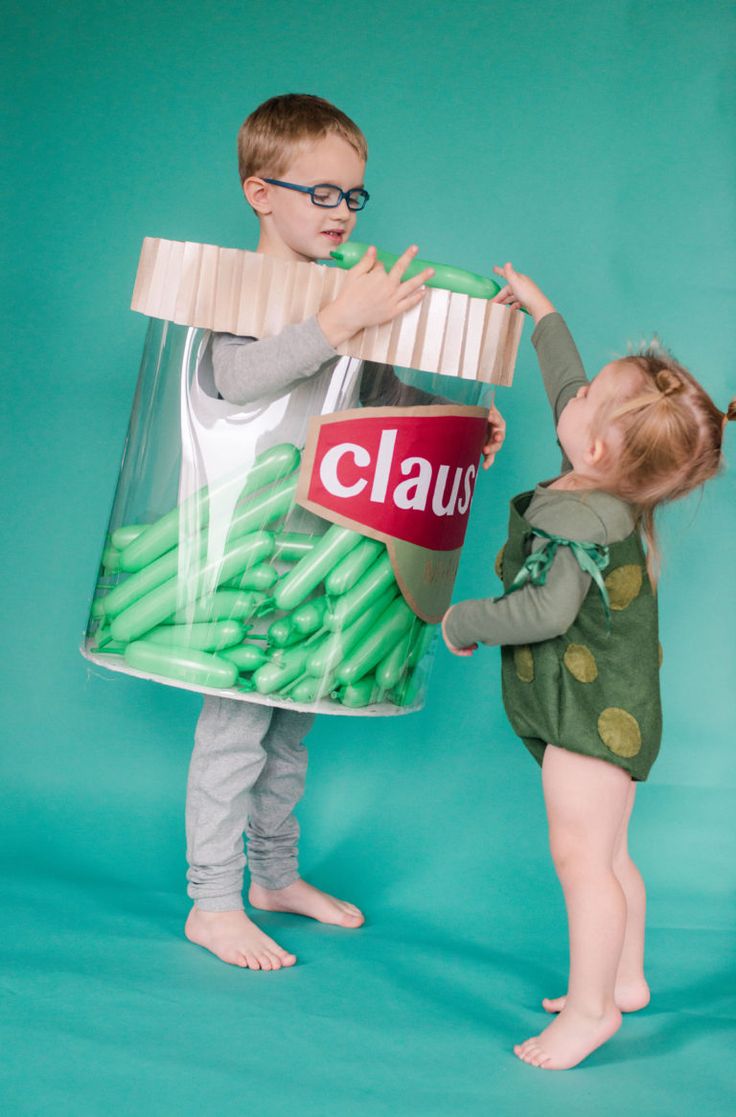 two young children standing next to each other in front of a bucket filled with green beans