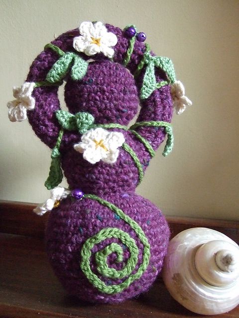 a purple crocheted vase with white flowers on it next to a seashell