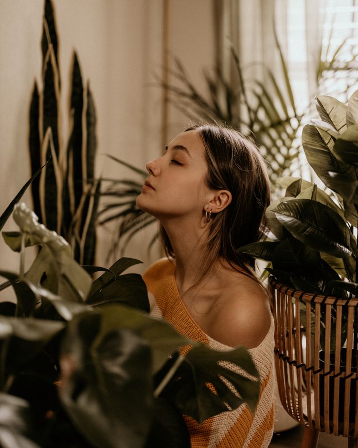 a woman is sitting in front of some plants and looking up at the sky with her eyes closed