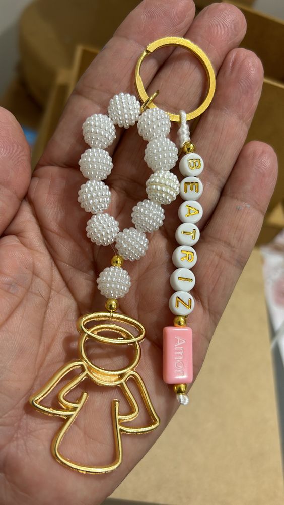 a hand holding a gold and white beaded keychain with an angel charm