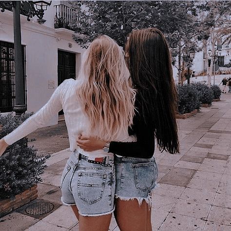 two young women are standing on the sidewalk and one is holding her hand out to another woman