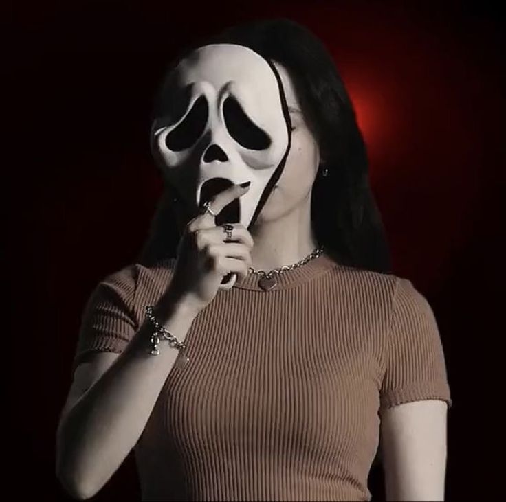 a woman wearing a white mask and holding her hand up to her mouth while standing in front of a red light