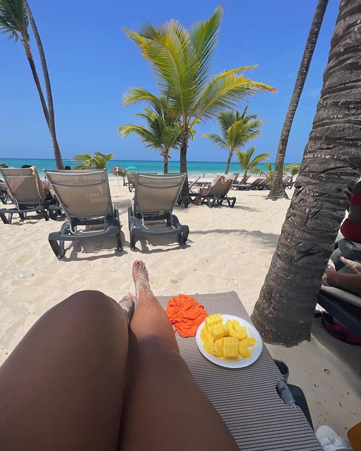 a woman laying on top of a sandy beach next to palm trees and eating fruit