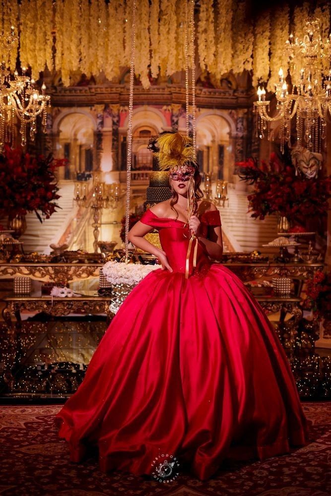 a woman in a red ball gown posing for the camera with a mask on her face