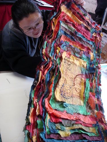 a woman is working on a piece of art made out of old clothes and fabrics