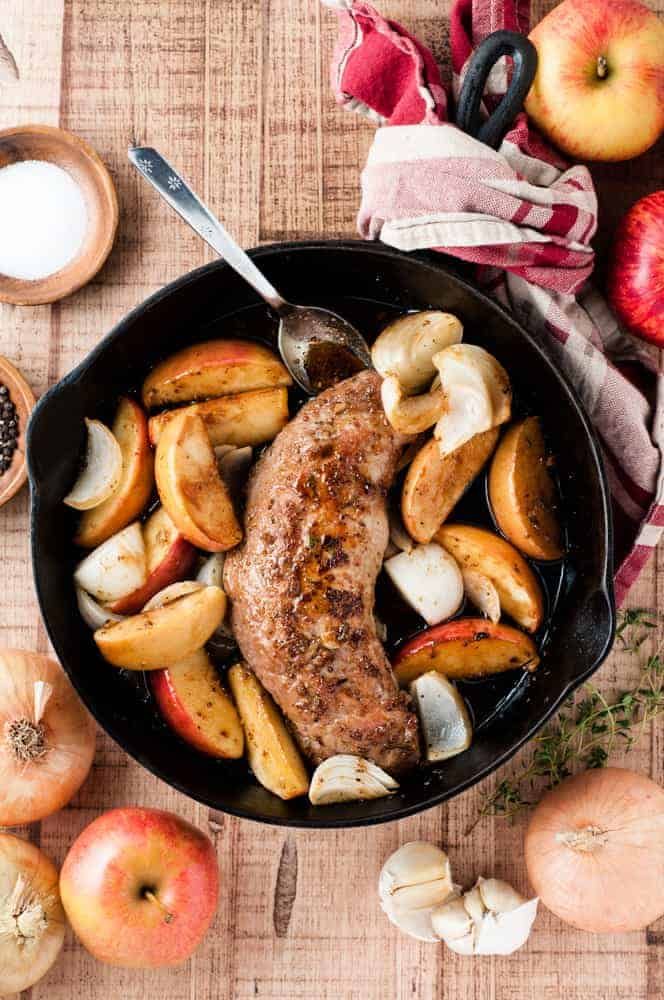 a skillet filled with meat and vegetables on top of a table next to apples