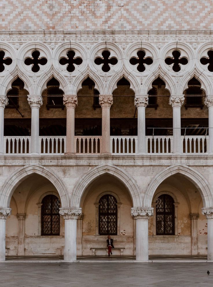 a woman in a pink dress is standing outside an old building with arches and columns