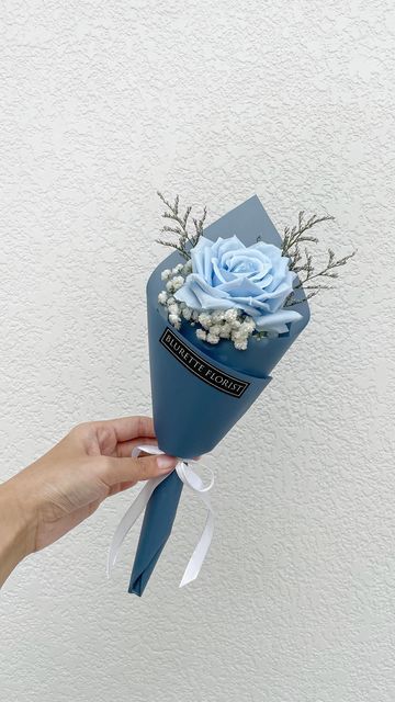 a hand holding a blue flower bouquet with white and blue flowers on it's side