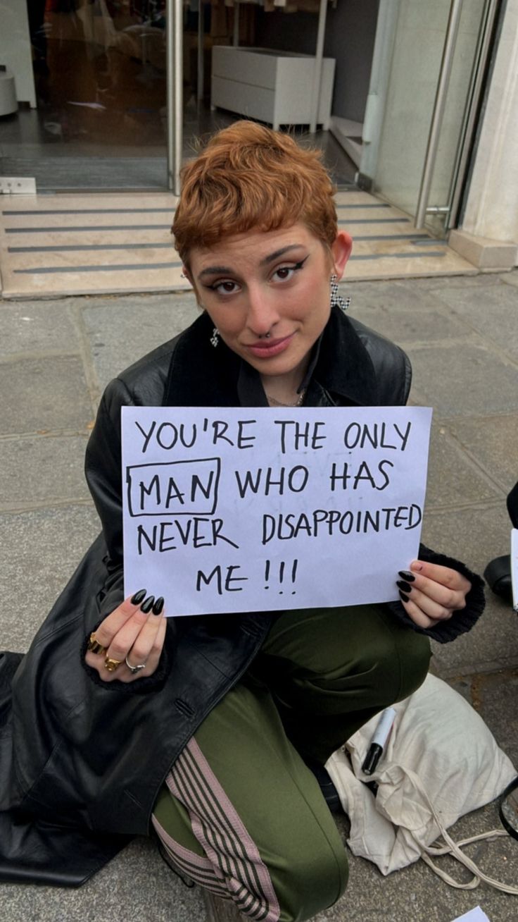 a woman sitting on the ground holding a sign