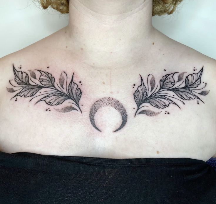 a woman's chest with two feathers and a crescent tattoo on the left side