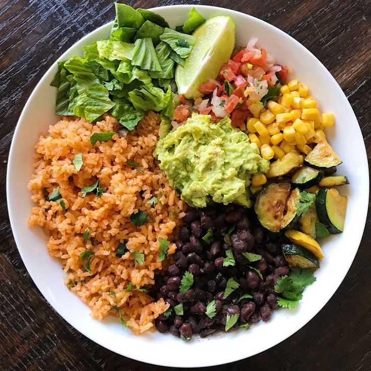 a white plate topped with rice, black beans and veggies next to avocado