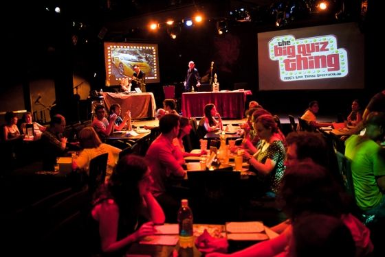 a group of people sitting at tables in front of a screen