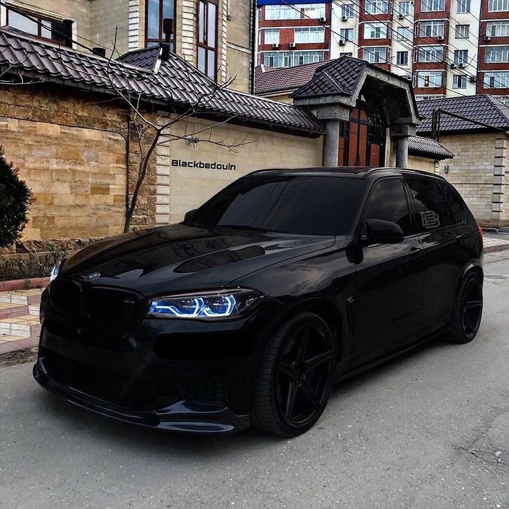 a black bmw is parked in front of a brick building with tall buildings behind it