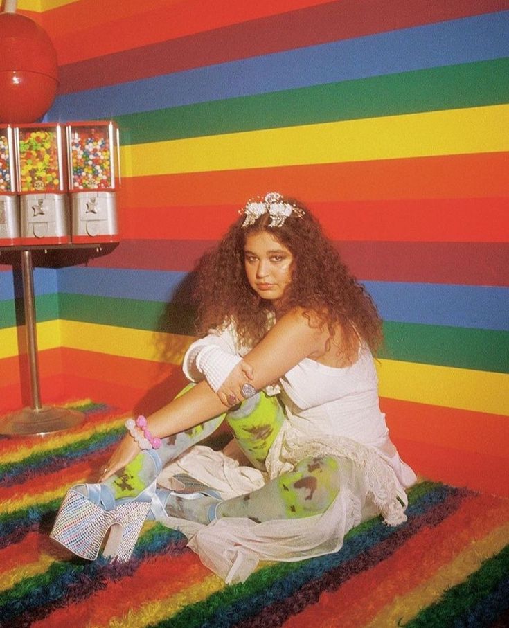 a woman sitting on top of a rainbow colored carpet next to a table filled with candy