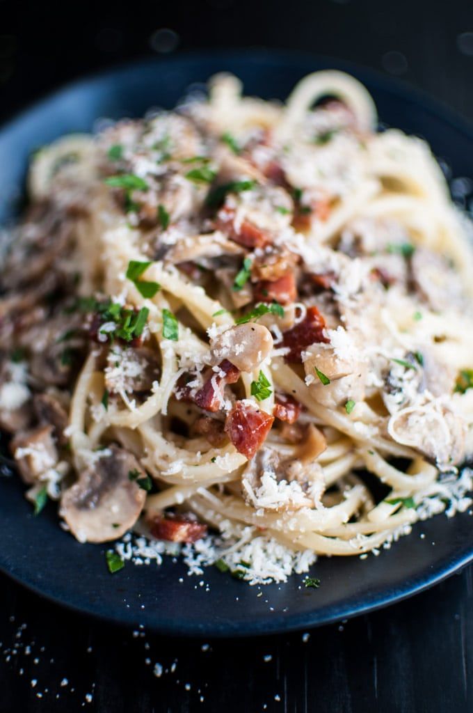 pasta with mushrooms, bacon and parmesan cheese on a blue plate sitting on a wooden table