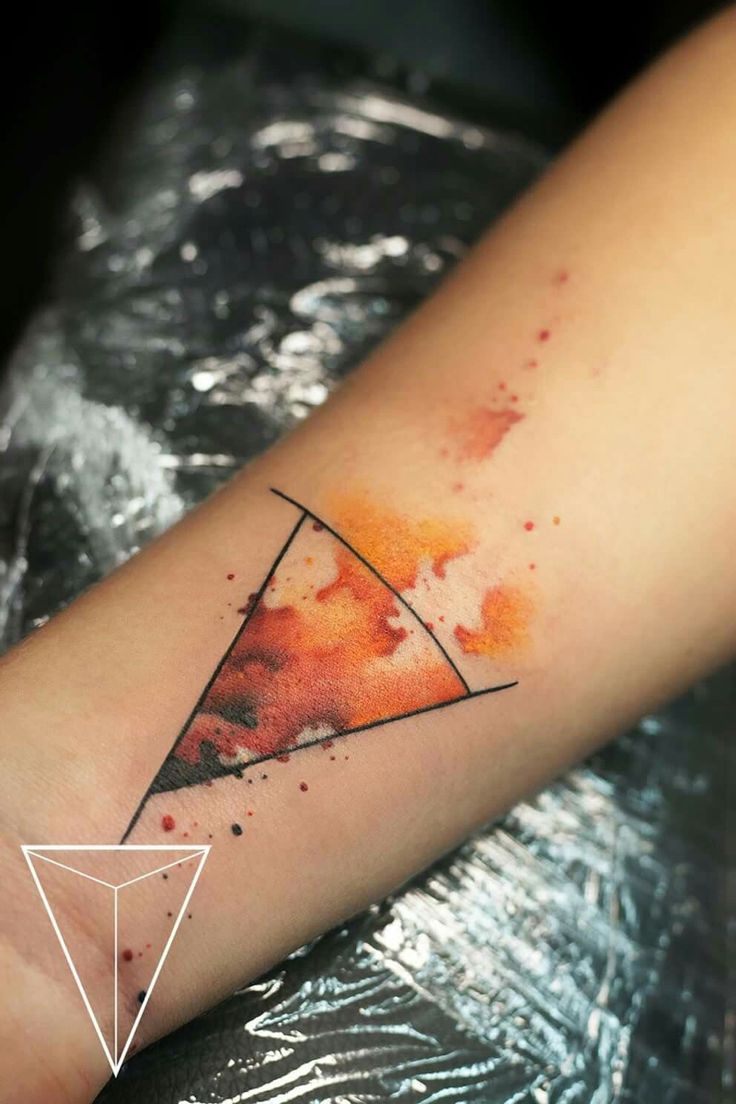 a watercolor tattoo on the arm with an orange and black triangle in front of it