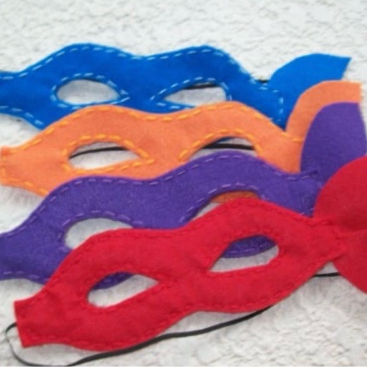 five different colored masks sitting on top of a white cloth covered table next to each other