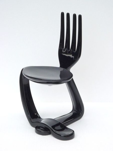 a black plastic chair with four forks sticking out of it's back end, against a white background