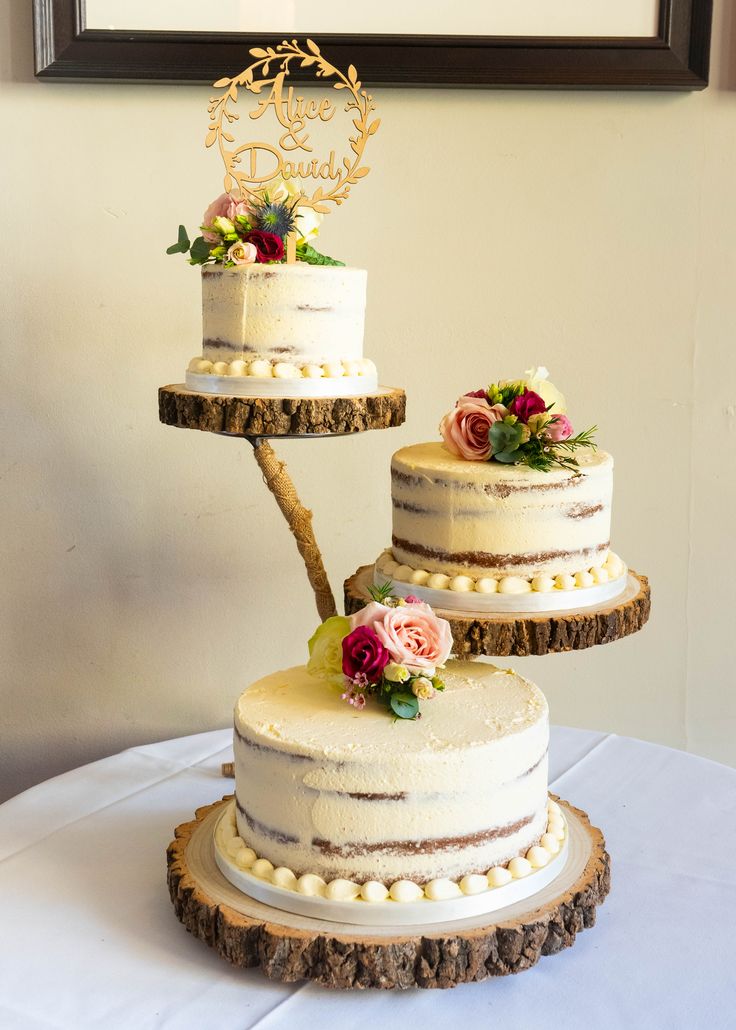 three tiered wedding cake with flowers on the top and one layer is decorated in wood