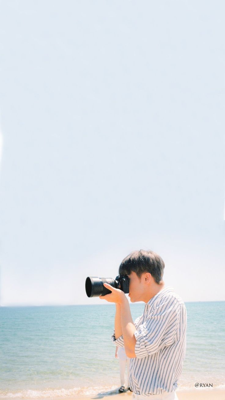 a man standing on top of a sandy beach next to the ocean holding a camera